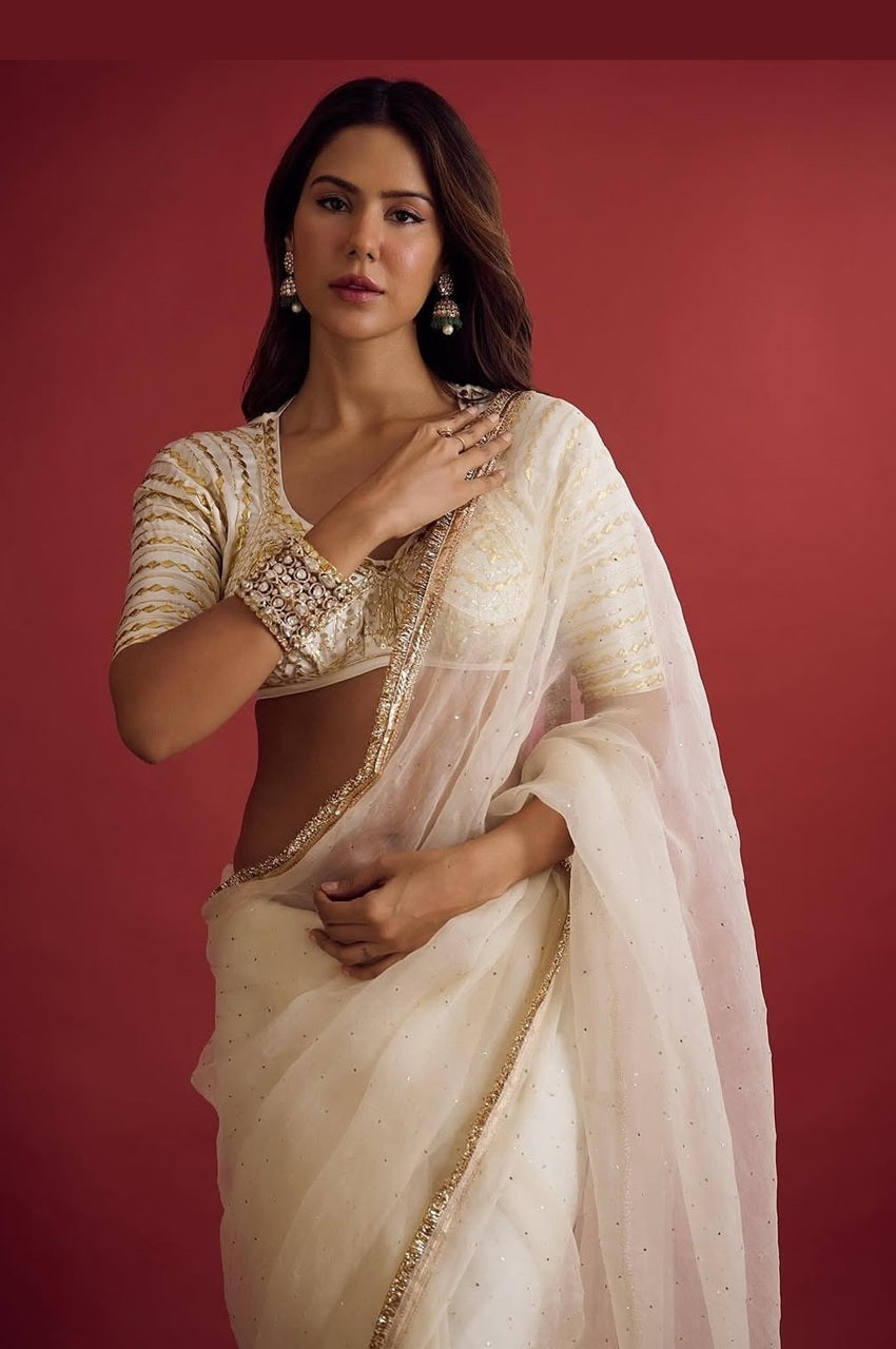 Woman wearing a white saree with gold details against a red background