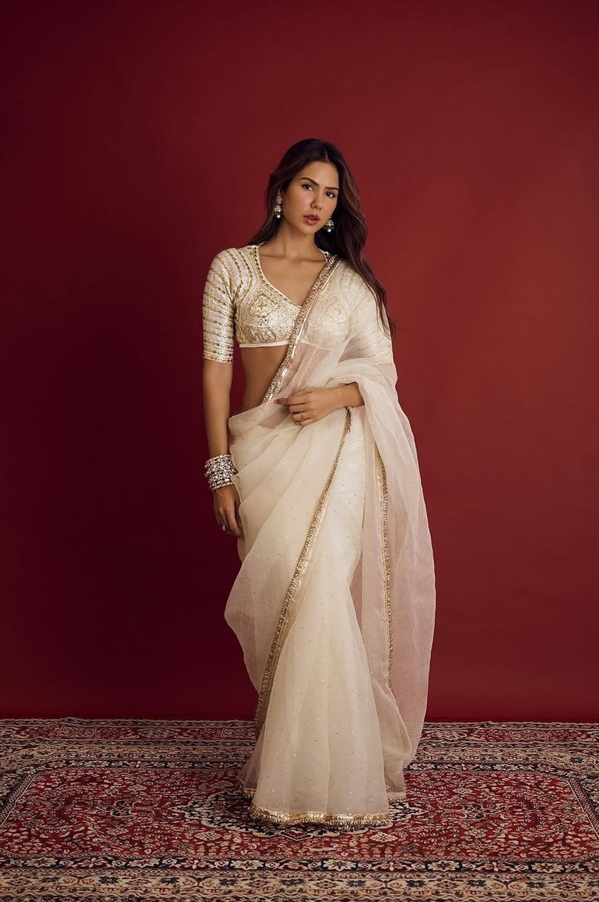 Woman in a white saree with gold details against a red background