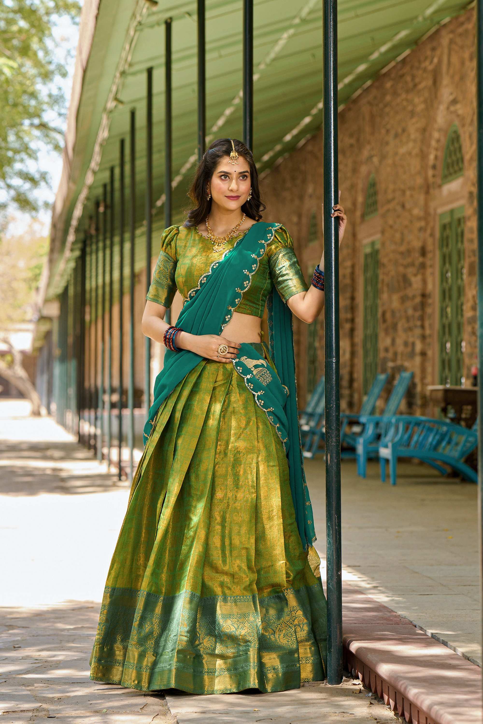 A woman elegantly dressed in a vibrant green and blue lehenga, showcasing intricate patterns and traditional style.