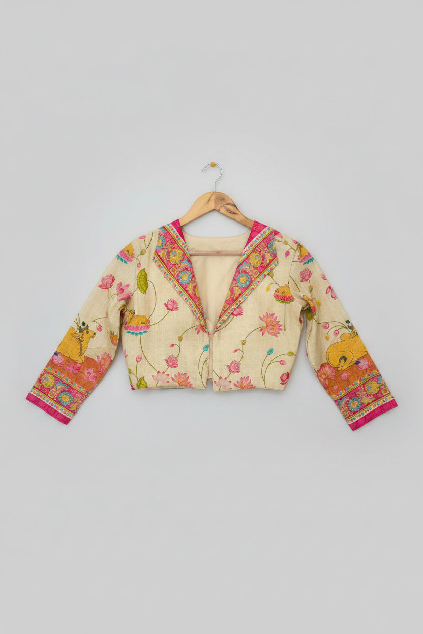 A cream-colored long-sleeve blouse with vibrant pink, orange, and green floral and cow prints, displayed on a wooden hanger over a white faux fur surface.