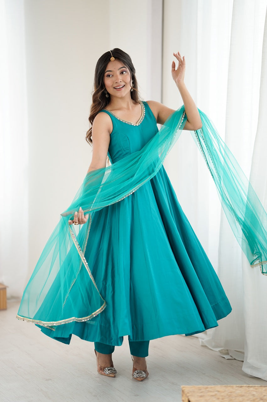 Woman in a teal traditional outfit with a matching dupatta against a white curtain background