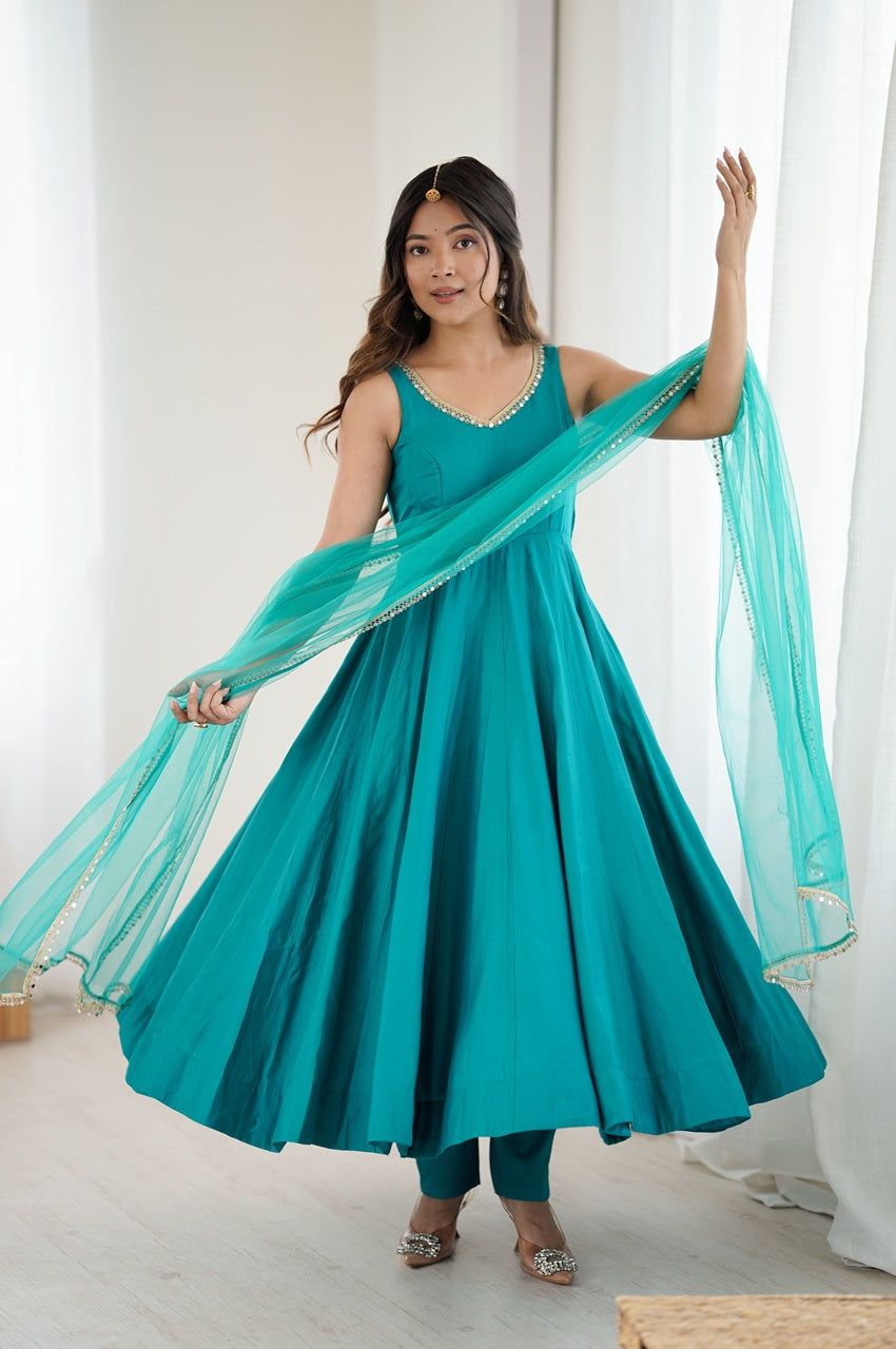 Woman in a teal dress with a matching dupatta standing against a white curtain background