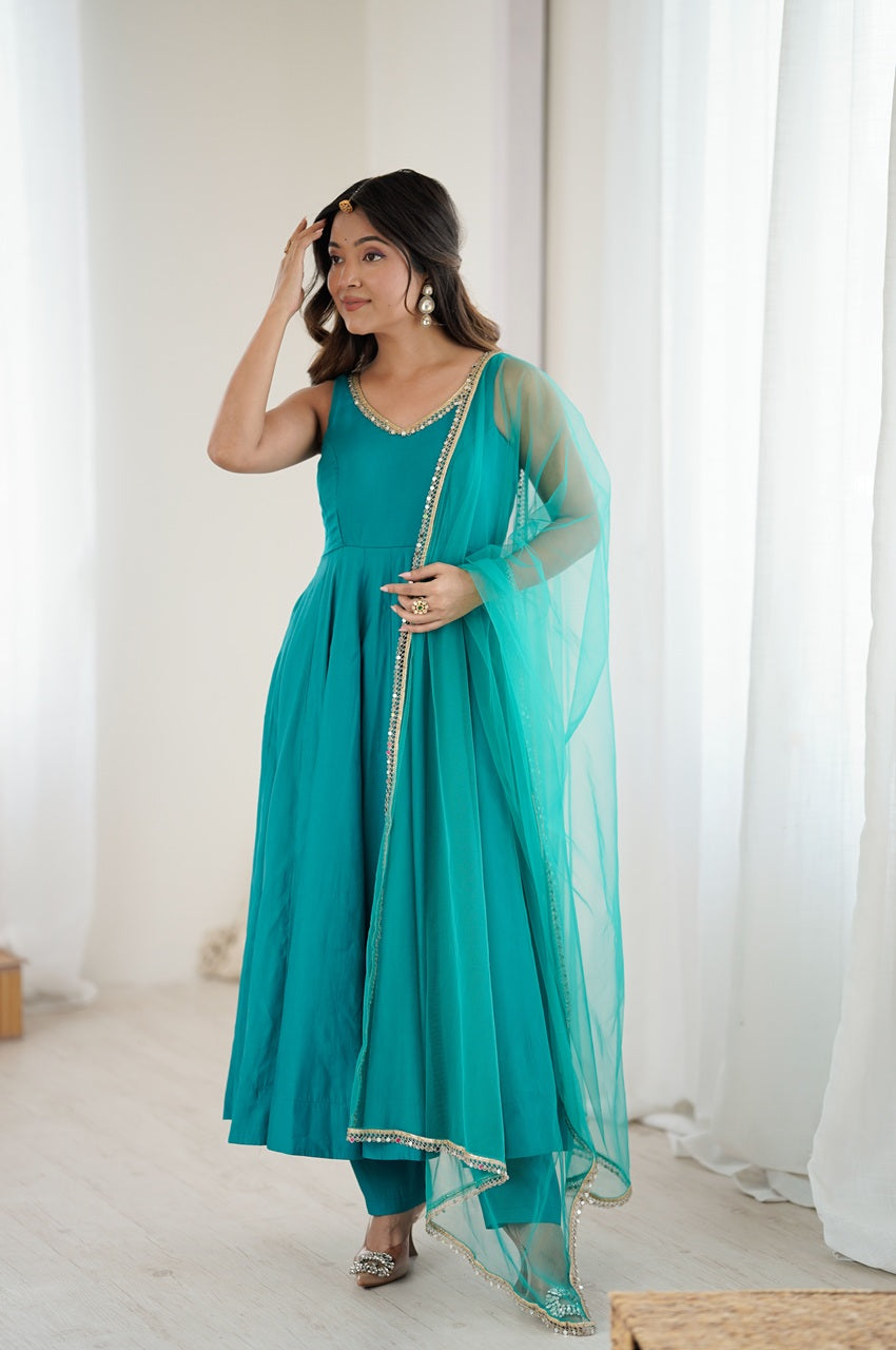 Woman wearing a teal traditional outfit with a sheer dupatta in a bright room.