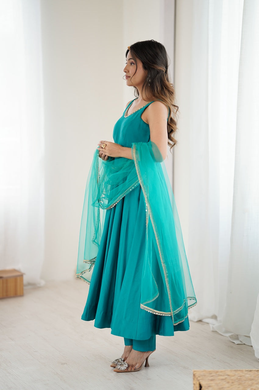 Woman wearing a teal traditional outfit with a matching dupatta in a bright room.