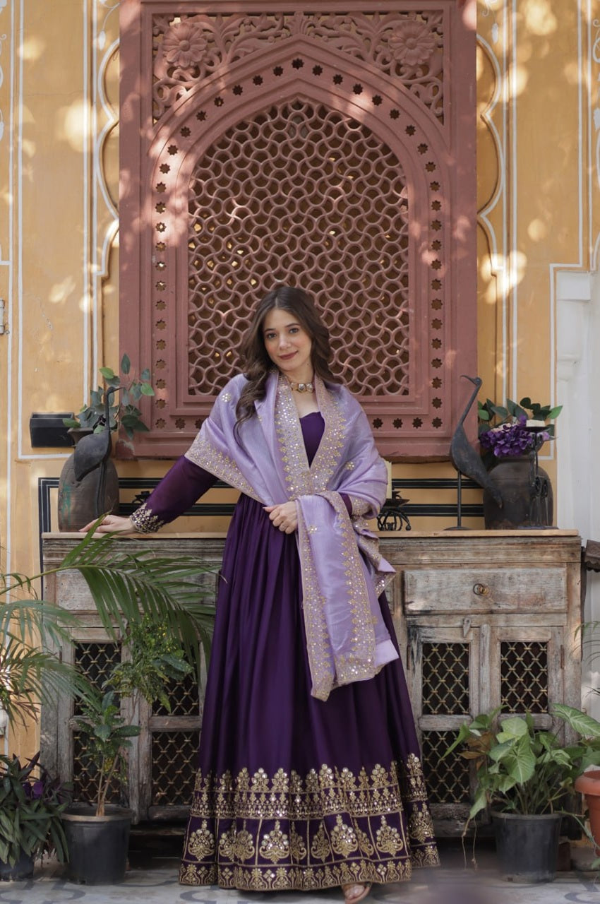 Woman in a purple traditional outfit standing in front of an ornate wooden screen with plants around.