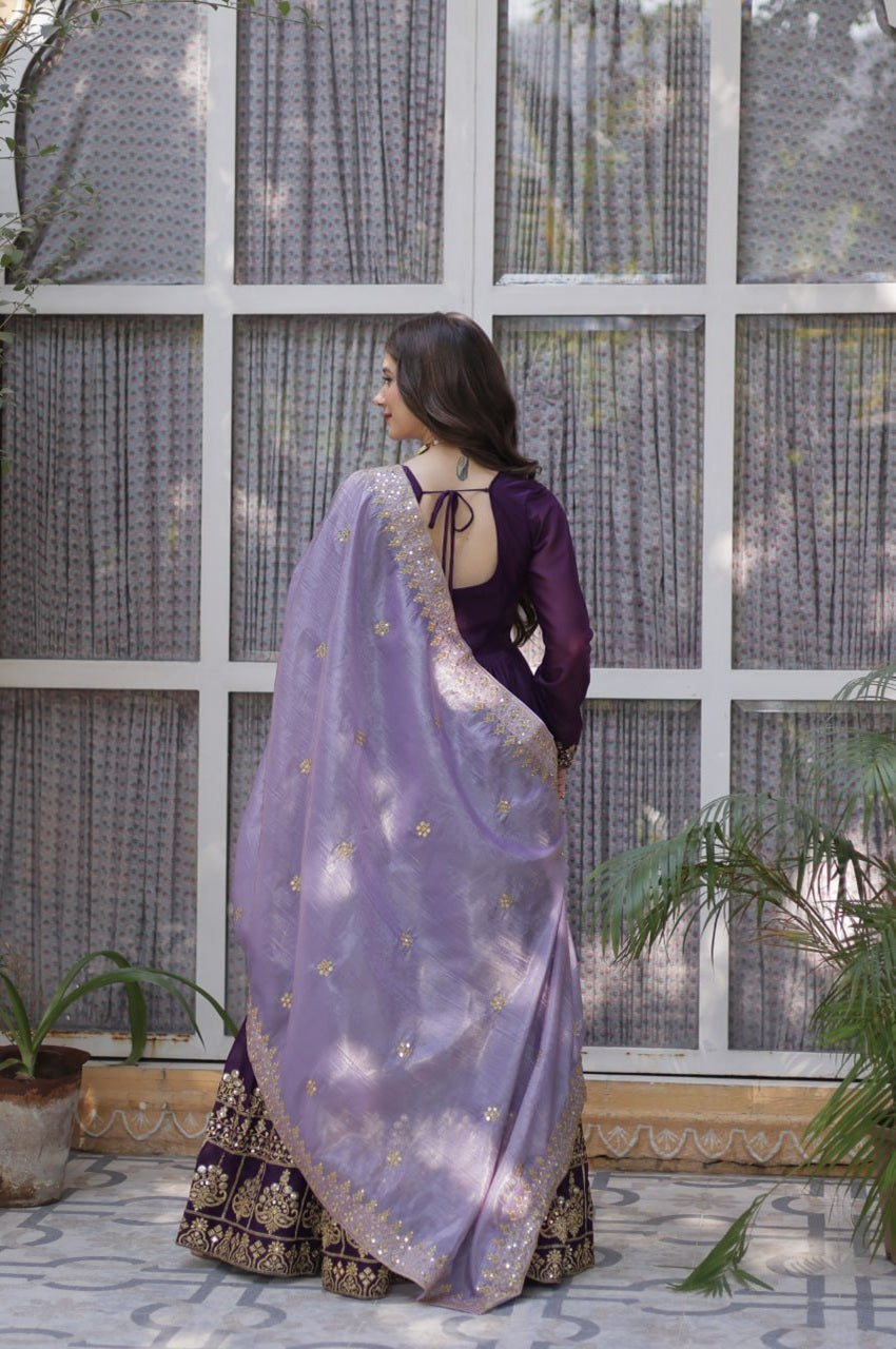 Woman in a purple saree with a floral pattern standing in front of a glass window.