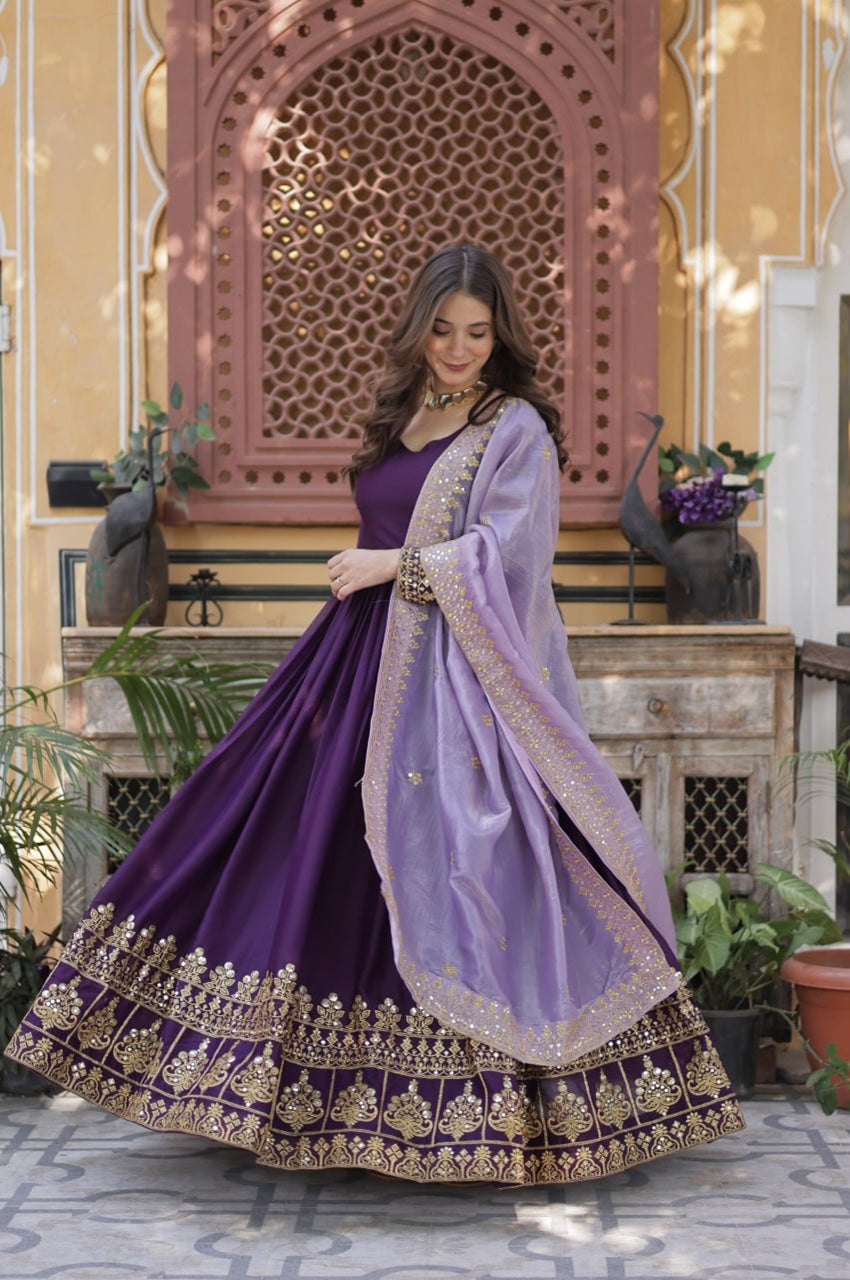 Woman in a traditional purple and lavender outfit with intricate designs, standing in an ornate indoor setting.