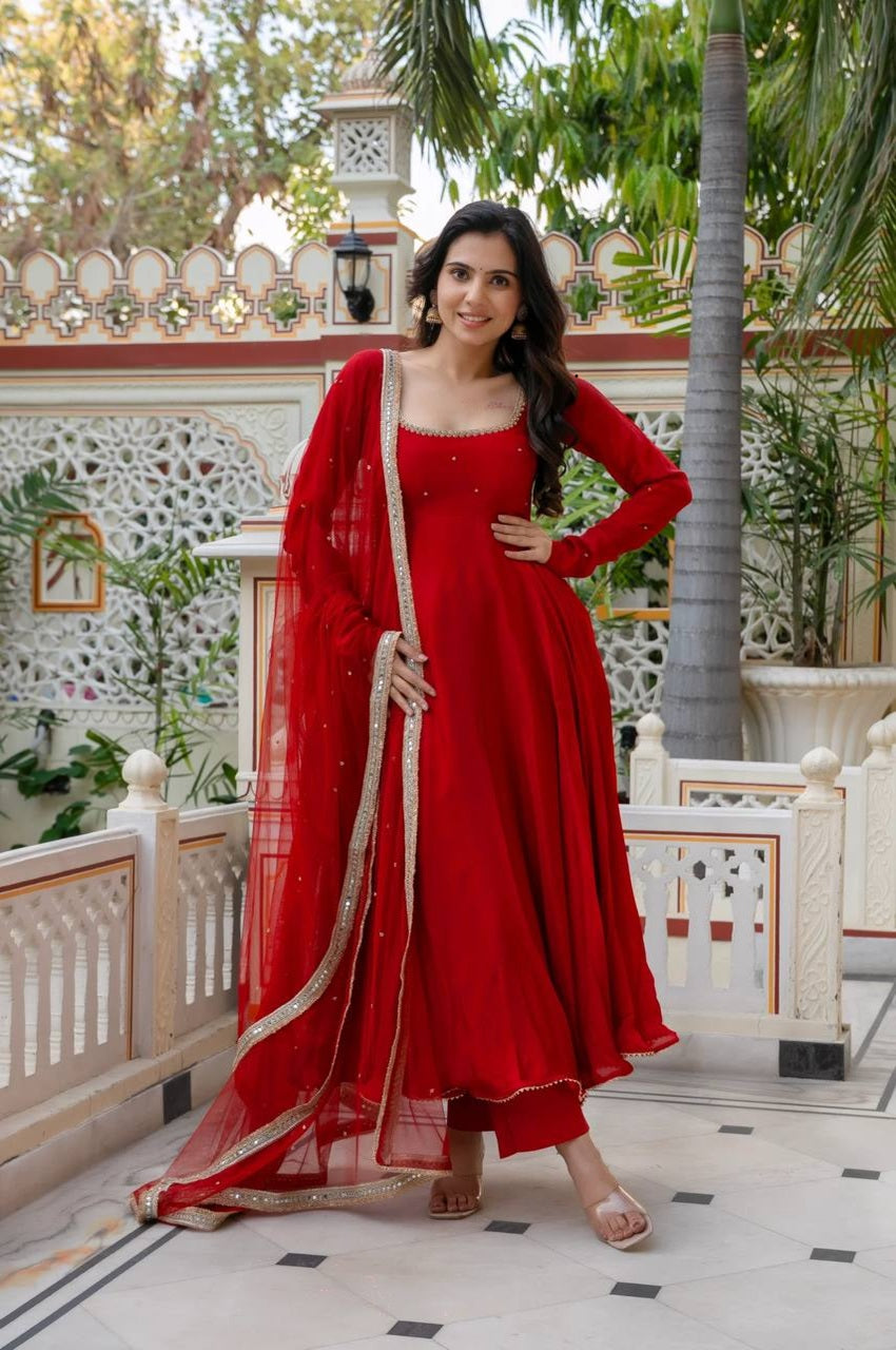 Woman in a red traditional outfit standing in an outdoor setting with greenery.