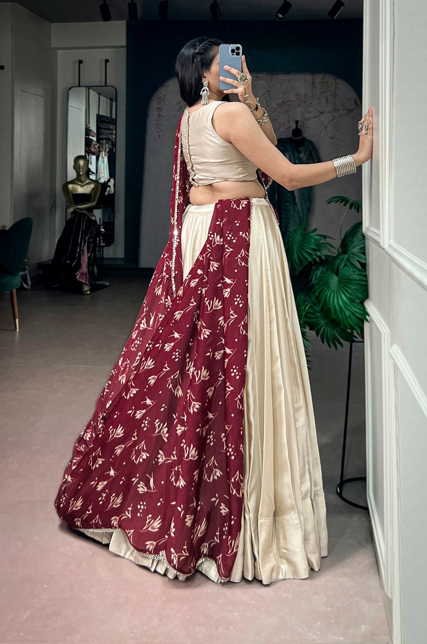 A woman takes a mirror selfie in a boutique wearing a traditional Indian lehenga choli outfit. The outfit features a deep maroon-red skirt with gold floral patterns, paired with a cream-colored satin skirt and a matching cream choli.