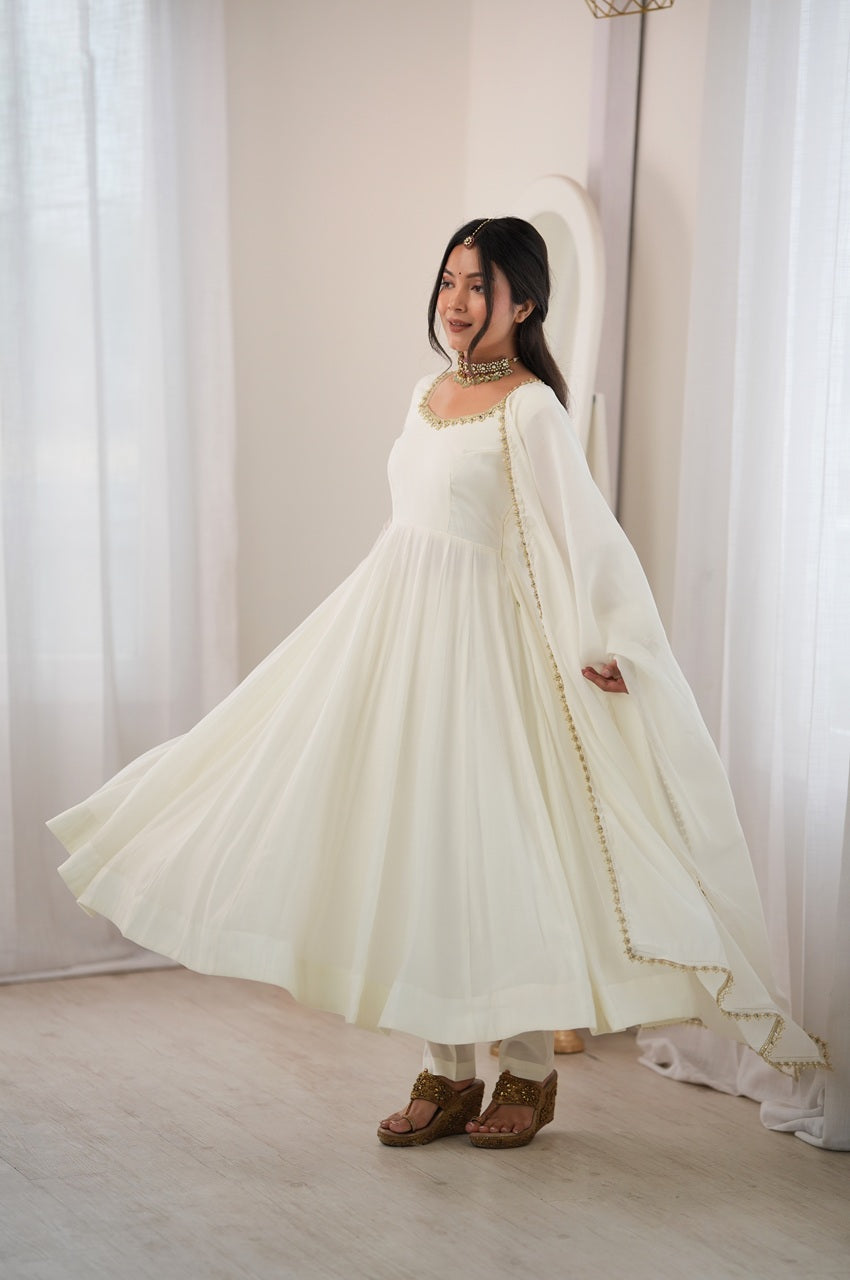 A woman wearing a flowing ivory white anarkali-style dress with gold embroidery and a matching sheer dupatta