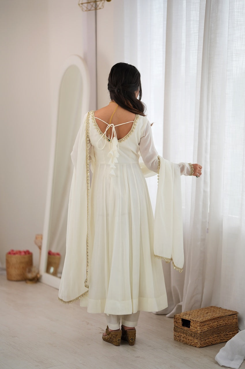A woman viewed from behind wearing a cream-colored traditional dress with a draped shawl, lace-up open back, and flared sleeves,