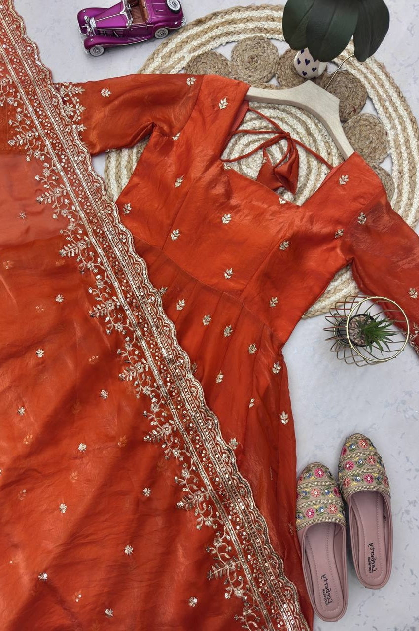 Orange traditional outfit with intricate embroidery, pink slippers, and decorative items on a textured surface.
