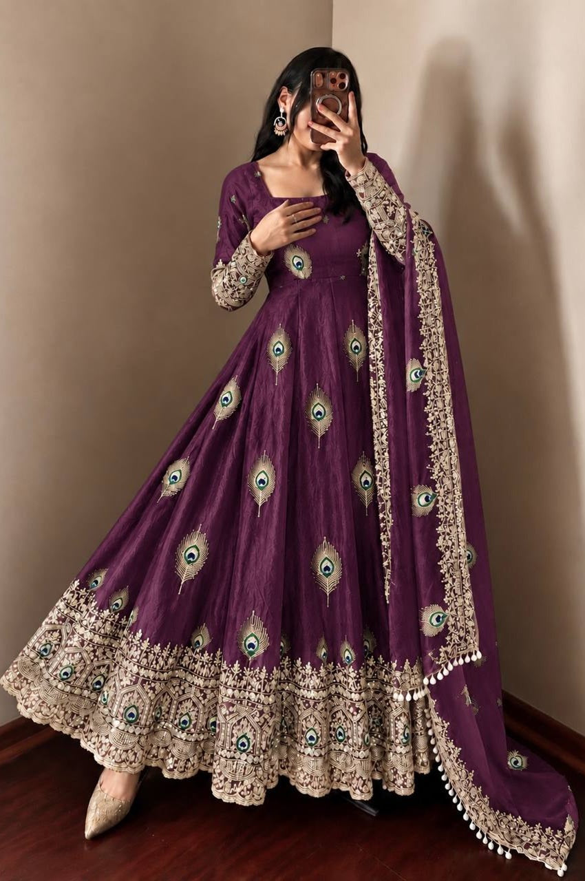 A woman takes a mirror selfie wearing a deep purple Anarkali gown with intricate gold embroidery, peacock feather motifs, and a matching embroidered dupatta.